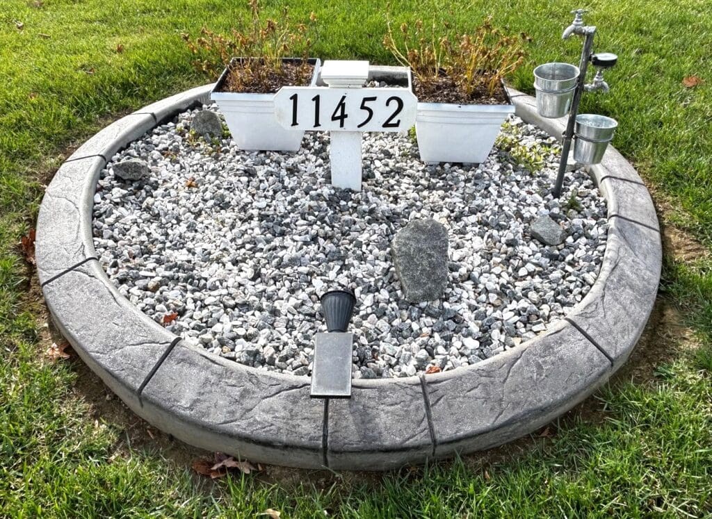 Decorative concrete landscape edging in Potomac, MD installed around a circular garden bed filled with white stone and ornamental grasses