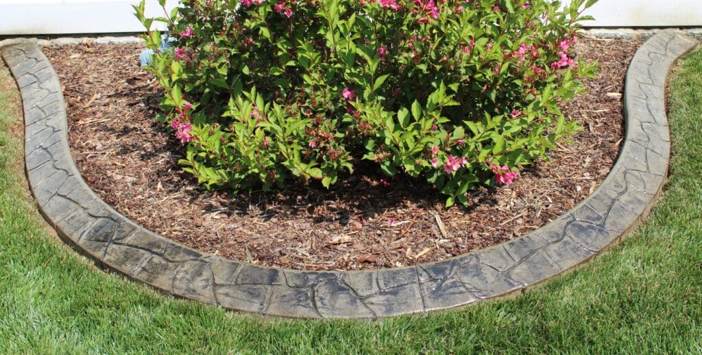 Decorative concrete landscape curbing forming a curved border around a flower bed with shrubs and mulch, creating clean edging for a residential yard in the DC metro area.