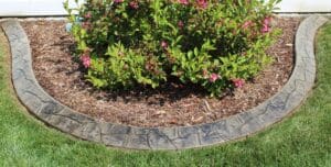 Decorative concrete landscape curbing forming a curved border around a flower bed with shrubs and mulch, creating clean edging for a residential yard in the DC metro area.