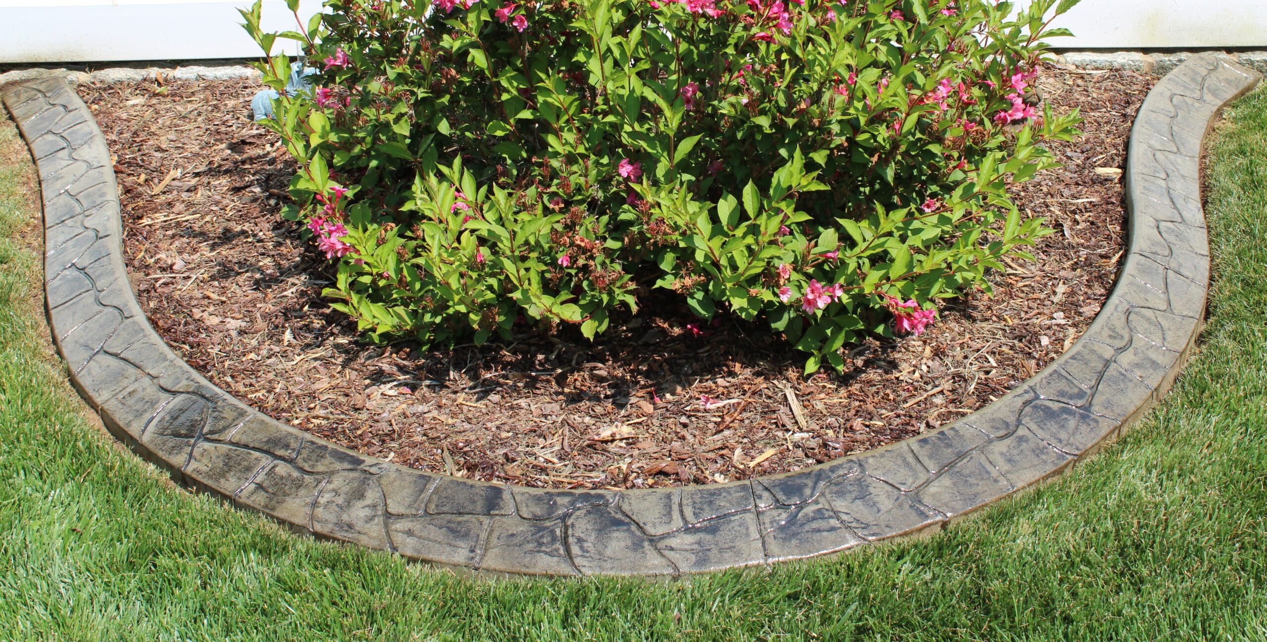 Decorative concrete landscape curbing forming a curved border around a flower bed with shrubs and mulch, creating clean edging for a residential yard in the DC metro area.